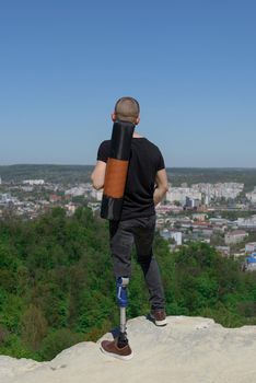 a man on a prosthetic leg travels the mountains. Dressed in black jeans and a T-shirt, he carrying mat.