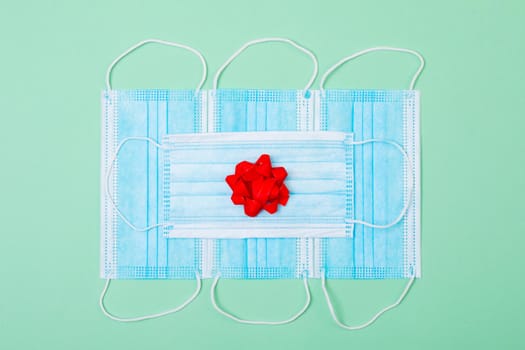 Composition of face masks with red ribbon on green background. christmas, tradition and celebration during coronavirus pandemic concept.