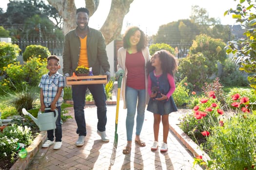 Happy african american family standing with garden tools and looking at camera. family time, having fun together at home and garden.