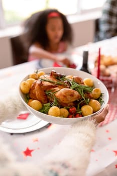 Hand of african american woman holding bowl with chicken and potatoes dish. christmas, festivity and tradition at home.