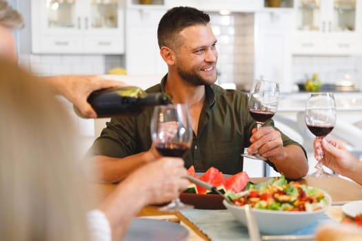 Caucasian grandfather and parents with son and daughter sitting at table and having dinner. family spending time together at home.