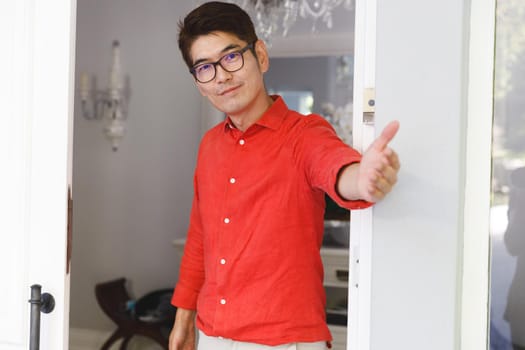 Portrait of smiling asian man standing at door and inviting visitor to room. hospitality and welcoming guests at home.
