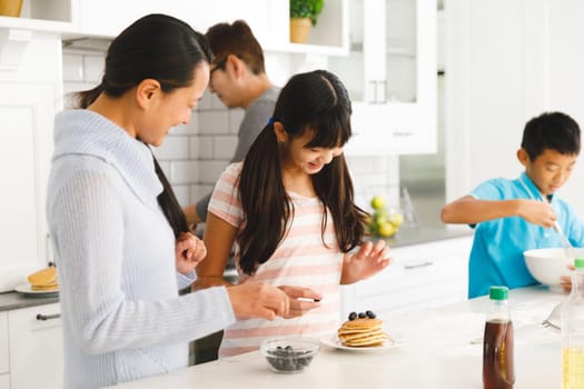 Happy asian parents with son and daughter preparing breakfast in kitchen. family enjoying preparing meal together at home.