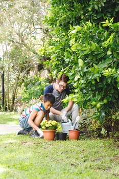 Happy asian father and son smiling, wearing gloves and planting plants together in garden. family leisure time at home gardening.