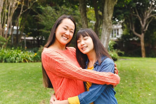 Portrait of happy asian mother embracing her daughter and smiling outdoors in garden. family enjoying leisure time together at home.