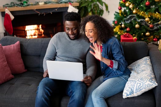 Happy african american couple having video call on laptop, christmas decorations in background. christmas, festivity and communication technology.