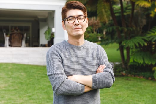 Portrait of happy asian man wearing glasses smiling in garden outside family home. enjoying leisure time alone at home.