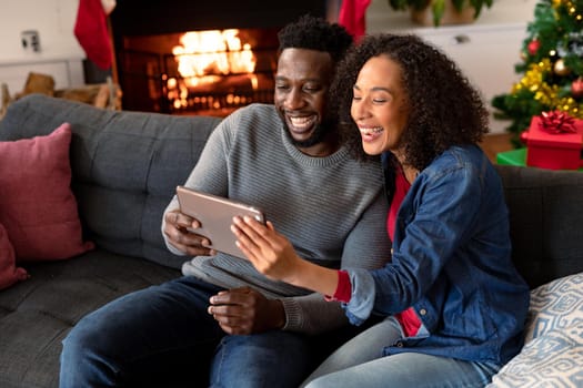 Happy african american couple having video call on tablet, christmas decorations in background. christmas, festivity and communication technology.