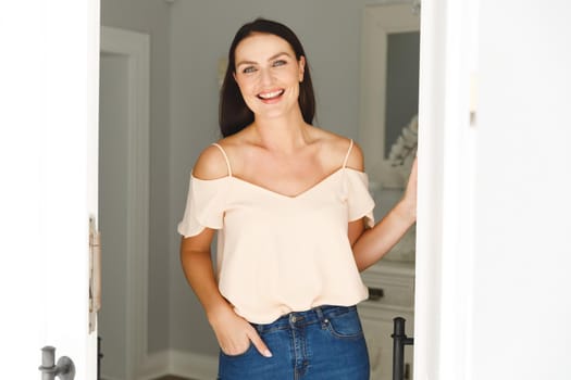 Portrait of happy caucasian woman standing at door, greeting a visitor and smiling. . hospitality and welcoming guests at home