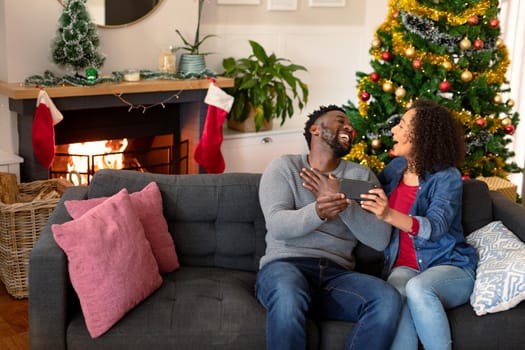 Happy african american couple having video call on smartphone, christmas decorations in background. christmas, festivity and communication technology.