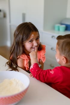 Portrait of happy, dirty with dough caucasian siblings baking in kitchen. cooking and baking, having fun with family at home.