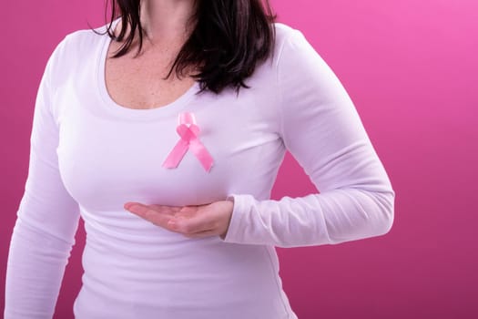 Midsection of caucasian woman in white tshirt with pink ribbon gesturing. breast cancer positive awareness campaign concept digitally generated video.