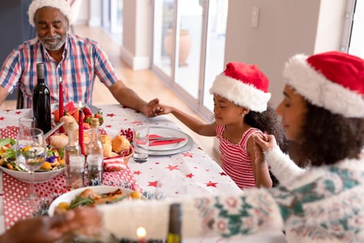 Happy multi generation family wearing santa hats, praying together, having christmas meal. family christmas time and festivity together at home.