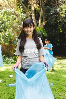 Portrait of smiling asian daughter putting rubbish in refuse sacks with family in the countryside. eco conservation volunteers, countryside clean-up.