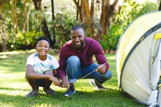 Portrait of african american father with son having fun and pitching tent in garden. family spending time at home.