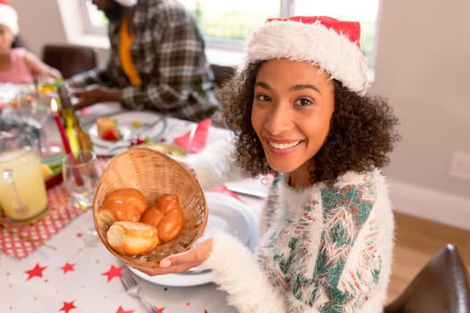 Smiling african american woman wearing santa hat holding basket with rolls. christmas, festivity and tradition at home.