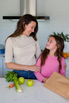 Happy caucasian mother and daughter unpacking groceries in kitchen. family time, having fun together at home.