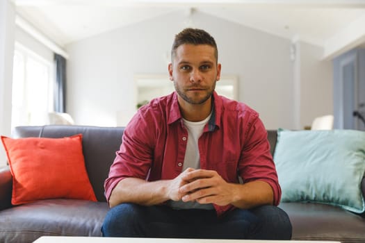 Caucasian man sitting on couch having video call in living room, sitting and listening. keeping in touch, at home with communication technology.