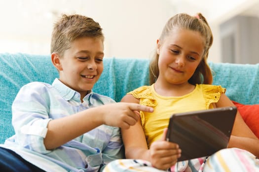 Happy caucasian brother and sister sitting on couch and using tablet in living room. childhood leisure time, fun and discovery at at home using technology.