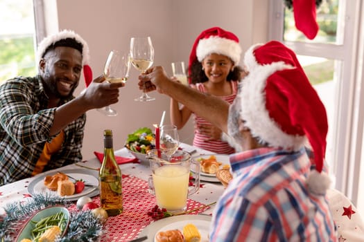 Happy multi generation family wearing santa hats, toasting with vine, having christmas meal. family christmas time and festivity together at home.