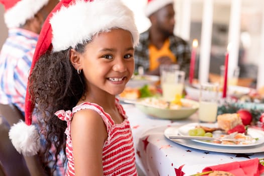 Happy african american girl wearing santa hat sitting at christmas table. family christmas time and festivity together at home.