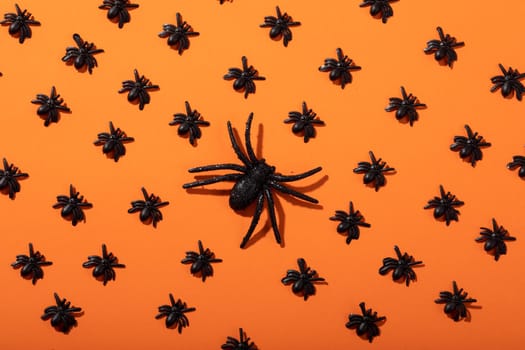 Composition of halloween decorations with rows of black spiders on orange background. halloween tradition and celebration concept.