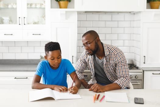 African american father and son in kitchen, doing homework together. family spending time at home, father son relationship.