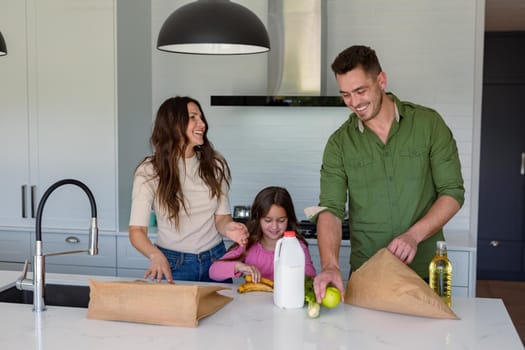 Happy caucasian parents and daughter unpacking groceries in kitchen. family time, having fun together at home.