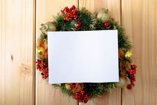Composition of white card with copy space framed with wreath on wooden background. christmas, tradition and celebration concept.