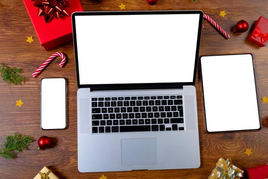 Composition of smartphone, laptop, tablet with copy space and decorations on wooden background. christmas, communication, tradition and celebration concept.