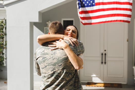 Caucasian male soldier hugging wife outside house decorated with american flag. soldier returning home to wife.