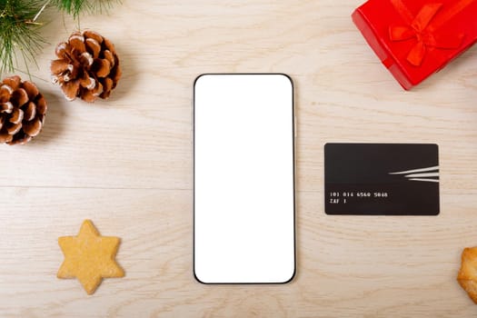 Composition of smartphone with copy space, card and christmas decorations on wooden background. christmas, communication, tradition and celebration concept.