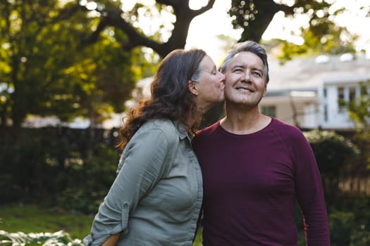 Happy senior caucasian couple kissing and smiling in garden. retirement lifestyle, spending time at home.