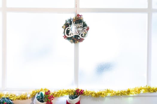Composition of merry christmas sign in window, with christmas stockings. christmas, tradition and celebration concept.
