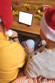 Father and two sons having a video call on digital tablet with copy space at home during christmas. social distancing during covid 19 pandemic at christmas time