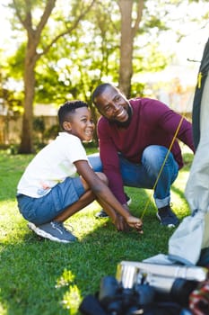 African american father with son having fun and pitching tent in garden. family spending time at home.