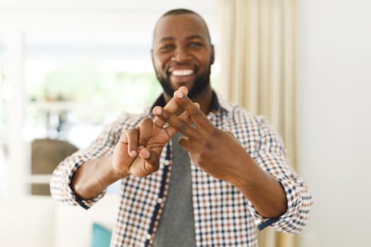 Portrait of african american man smiling and looking at camera in living room talking sign language. communication without words.