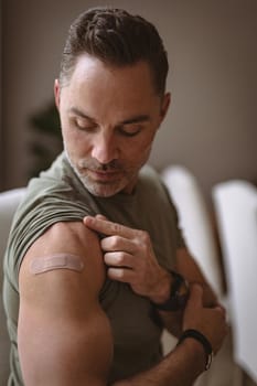 Caucasian man showing his vaccinated shoulder at home. vaccination for prevention of coronavirus outbreak concept