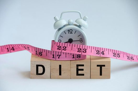 Diet text on wooden blocks with alarm clock tied with measuring tape. Weight loss and fitness concept