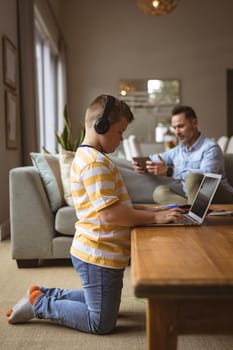 Caucasian boy wearing headphones using laptop in the living room at home. home schooling and education concept