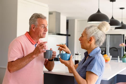 Caucasian senior couple drinking coffee together and talking in kitchen. healthy retirement lifestyle at home.