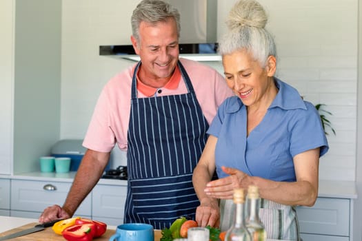 Happy caucasian senior couple standing in kitchen and preparing meal together. healthy retirement lifestyle at home.