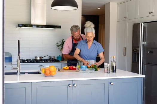 Happy caucasian senior couple standing in kitchen and preparing meal together. healthy retirement lifestyle at home.