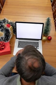 Caucasian senior man having video call on laptop with copy space at christmas time. christmas, festivity and communication technology at home.