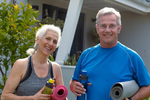 Happy caucasian senior couple holding yoga mats and looking at camera. active and healthy retirement lifestyle at home and garden.