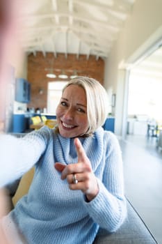 Happy senior caucasian woman in living room sitting on sofa, making video call. retirement lifestyle, at home with technology.