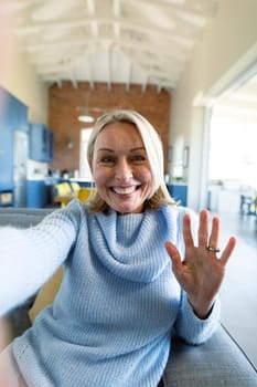 Happy senior caucasian woman in living room sitting on sofa, making video call. retirement lifestyle, at home with technology.