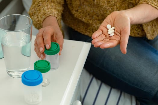 Hands of caucasian senior woman taking pills and sitting on bed. senior health and lifestyle at home.