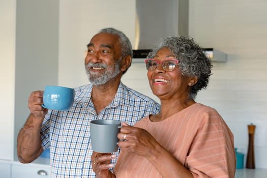 Happy african american senior couple holding mugs with coffee and talking. healthy retirement lifestyle at home.