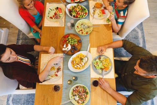 Overhead view of caucasian parents with son and daughter sitting at table and having dinner. family spending time together at home.